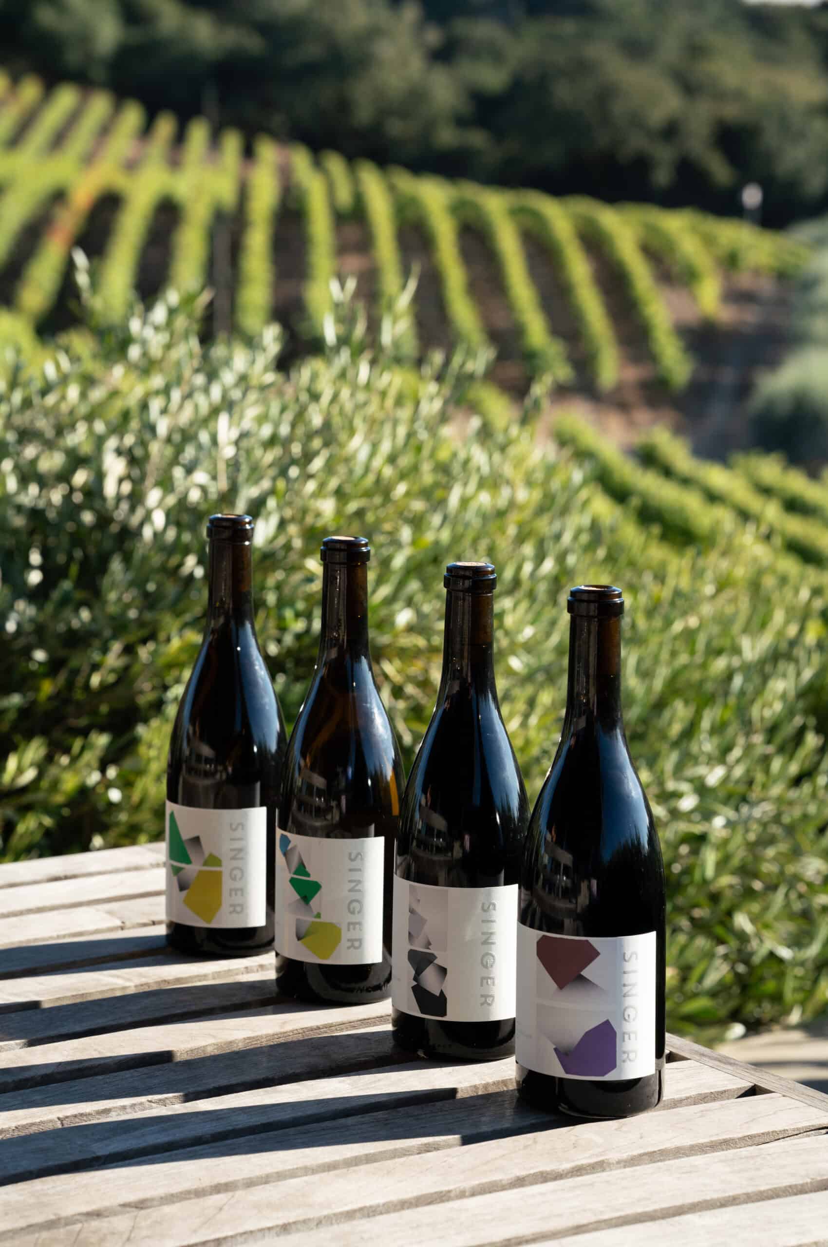 Bottles of Singer Wine on wooden table in a vineyard setting, showcasing premium wine for enthusiasts.