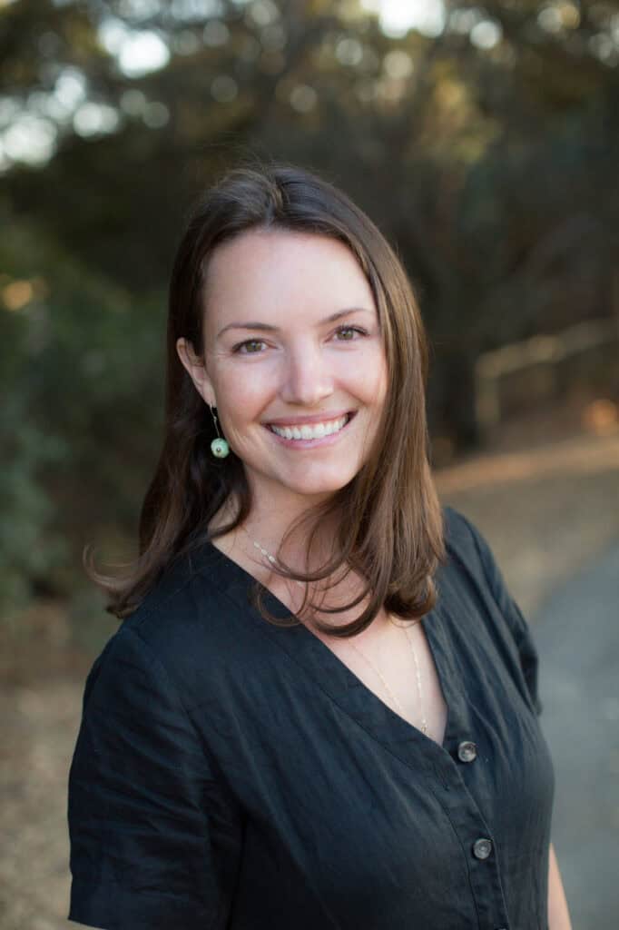 Bright woman smiling outdoors holding Singer Wine, natural light, nature background, showcasing wine and lifestyle.